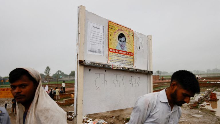 People stand near a poster of preacher Surajpal, also known as 'Bhole Baba' stuck on a board, at the site where believers had gathered for a Hindu religious congregation following which a stampede occurred, in Hathras district of the northern state of Uttar Pradesh, India, July 3, 2024. REUTERS/Anushree Fadnavis