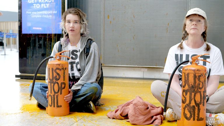 Two women stage a protest sitting in the orange paint they sprayed on the floor at Terminal 5. Pic: Just Stop Oil
