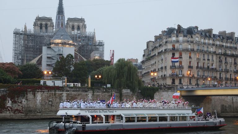 Olympic delegates wave flags as they travel past Notre Dame on the way to the opening ceremony in Paris. Pic: Reuters