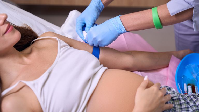 Cropped image of female nurse preparing hand of young pregnant woman to injection on medical bed in hospital. Concept of pregnancy and maternity