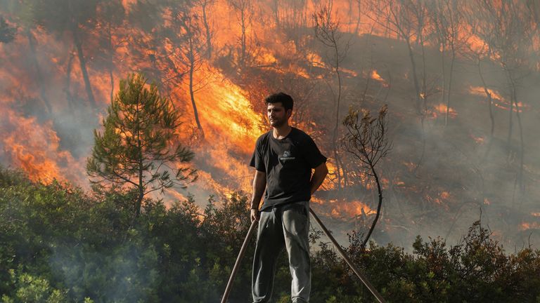 Ein Freiwilliger steht auf dem Dach eines Gebäudes, während in Stamata die Flammen eines verheerenden Feuers aufsteigen.  Foto: Reuters