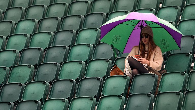 A spectator shelters under an umbrella as rain falls on day five of the 2024 Wimbledon Championships at the All England Lawn Tennis and Croquet Club, London. Picture date: Friday July 5, 2024.