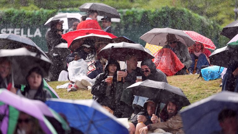 Spectators on the hill shelter from the rain under umbrellas on day six of the 2024 Wimbledon Championships at the All England Lawn Tennis and Croquet Club, London. Picture date: Saturday July 6, 2024.