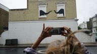 A woman stops to photograph a new artwork depicting two elephants poking their heads out of blocked out windows unveiled by Banksy on the side of a building at the junction of Edith Grove and Edith Terrace, in Chelsea, south west London. Picture date: Tuesday August 6, 2024.