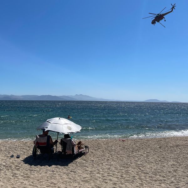 A helicopter flies over a beach in Greece as authorities tackle wildfires. Pic: Florian Neuhof