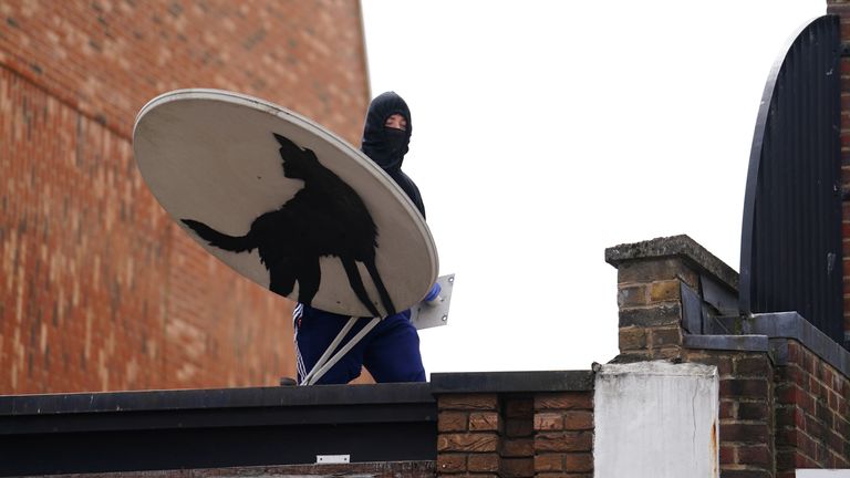 People remove a new artwork by Banksy, depicting a howling wolf painted on a satellite dish that was placed on a shop roof in Peckham, south London. The artist’s latest artwork comes a day after he unveiled three monkeys painted on a bridge in Brick Lane, east London. Picture date: Thursday August 8, 2024.

 eiqekiqkhiqkhinv