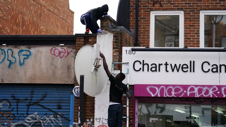 People remove a new artwork by Banksy, depicting a howling wolf painted on a satellite dish that was placed on a shop roof in Peckham, south London. The artist’s latest artwork comes a day after he unveiled three monkeys painted on a bridge in Brick Lane, east London. Picture date: Thursday August 8, 2024.

