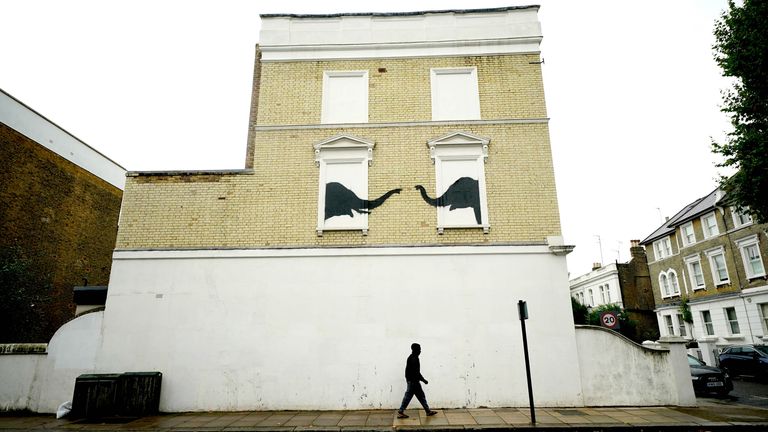 A man passes underneath a new artwork depicting two elephants poking their heads out of blocked out windows unveiled by Banksy on the side of a building at the junction of Edith Grove and Edith Terrace, in Chelsea.
Pic:PA