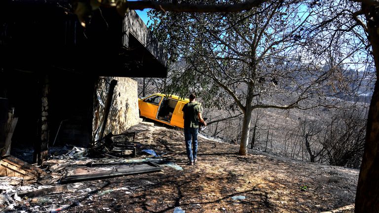 A man walks next to a burned house as a wildfire burns near the village of Varnavas.
Pic: Reuters