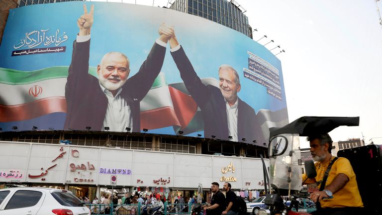 Vehicles drive past a huge banner showing the late Hamas leader Ismail Haniyeh, left, who was killed in an assassination last week, joining hands with Iranian President Masoud Pezeshkian, in a square in downtown Tehran, Iran, Monday, Aug. 5, 2024. Iran has vowed to respond with "power and decisiveness" to the targeted killing of Hamas' top political leader, which it blamed on Israel. (AP Photo/Vahid Salemi)