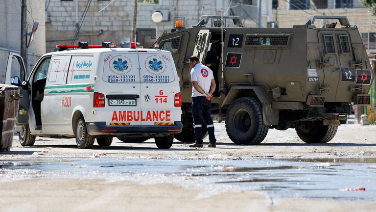 An ambulance crew member stands next to an ambulance and an Israeli military vehicle, during a raid, in Jenin, in the Israeli-occupied West Bank, August 28, 2024. REUTERS/Raneen Sawafta