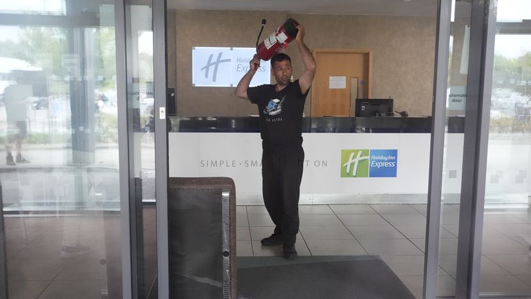 A man holds a fire extinguisher in the lobby of the hotel as seen through closed glass doors as trouble flares during an anti-immigration protest outside the Holiday Inn Express in Rotherham, South Yorkshire. Picture date: Sunday August 4, 2024.