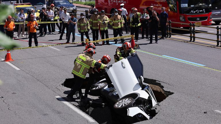 South Korean firefighters check a vehicle that fell into a sinkhole on a street in Seoul, South Korea.
Pic:Yonhap/AP