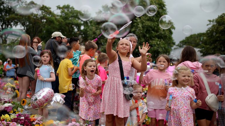 Children play with bubble wands among floral tributes left outside Town Hall in Southport ahead of a vigil in memory of three children who died in a 'ferocious' attack.  knife attack during a Taylor Swift event at a dance school last Monday.  Photo date: Monday, August 5, 2024.