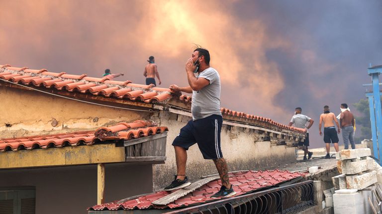 People stand on the roof of a building as smoke rises from a wildfire burning in Vrilissia, near Athens, Greece, August 12, 2024. REUTERS/Alexandros Avramidis