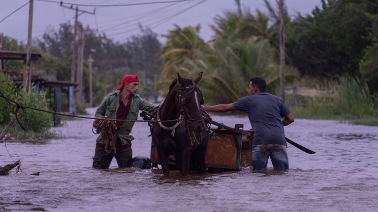 People traverse a flooded street with a horse-drawn carriage after the passage of Hurricane Helene in Guanimar, Artemisa province, Cuba, Wednesday, Sept. 25, 2024. (AP Photo/Ramon Espinosa)