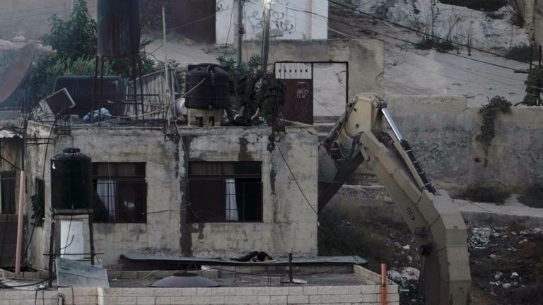 Israeli soldiers look over a rooftop where two lie motionless in the West Bank town of Qabatiya. Pic: AP