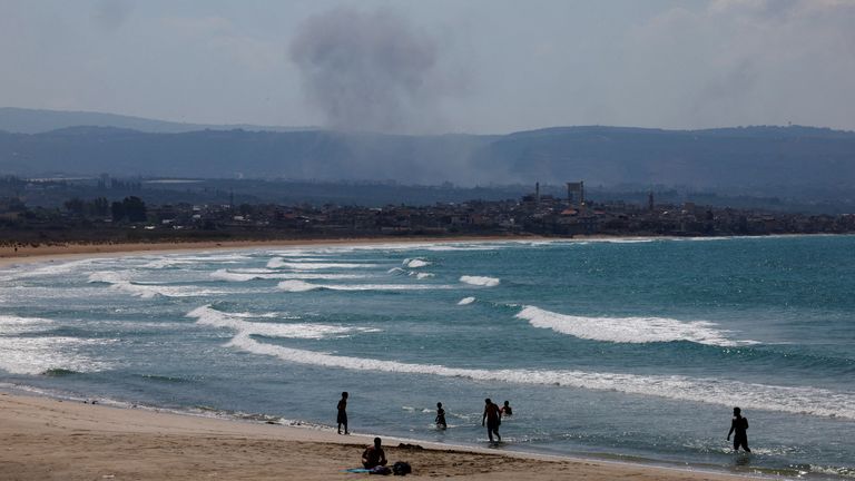 People spend time at the beach as smoke billows over southern Lebanon amid the cross-border clashes this week. Pic: Reuters