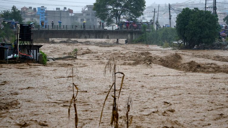 Ludzie obserwują z mostu wzburzone wody rzeki Bagmati, gdy rzeka wylała z powodu ulewnych deszczy w Katmandu w Nepalu, sobota, 28 września 2024 r. (AP Photo/Gopen Rai)