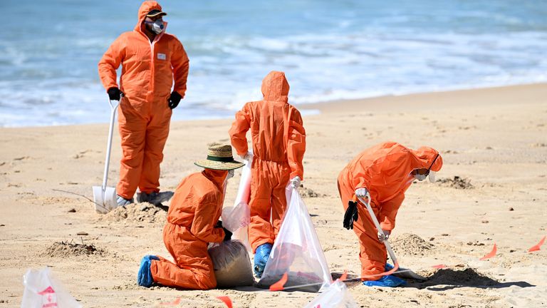 Trabalhadores com roupas de proteção limpam detritos desconhecidos encontrados na praia de Coogee.  Foto: AAP/Reuters