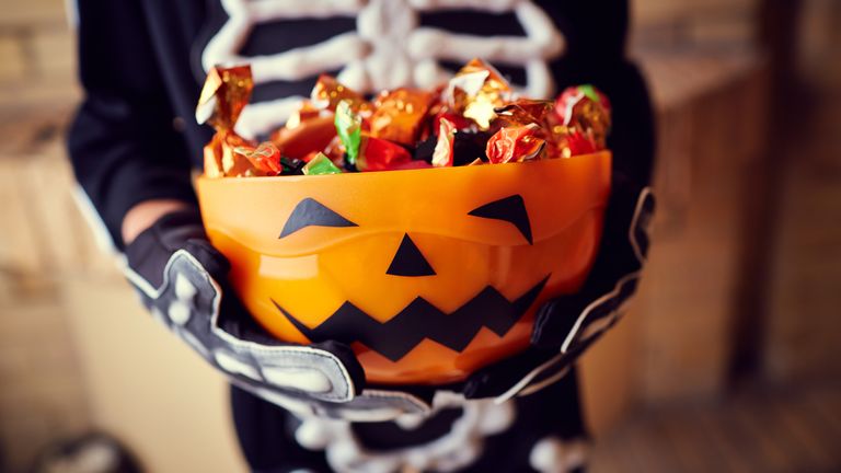 Boy in skeleton costume holding bowl full of candies 