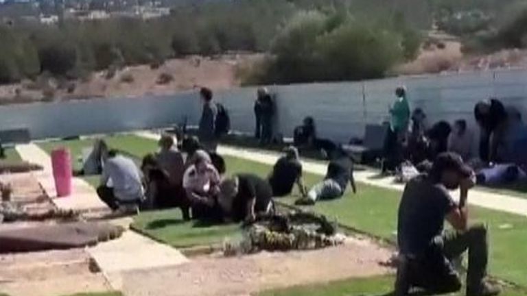 Mourners in northern Israel lie on the ground at a cemetery as sirens wail after rocket launch
