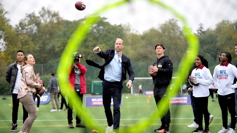 The Prince of Wales throws a football at a target, watched by Louis Rees-Zammit, left, as he attends a NFL Foundation Flag event.