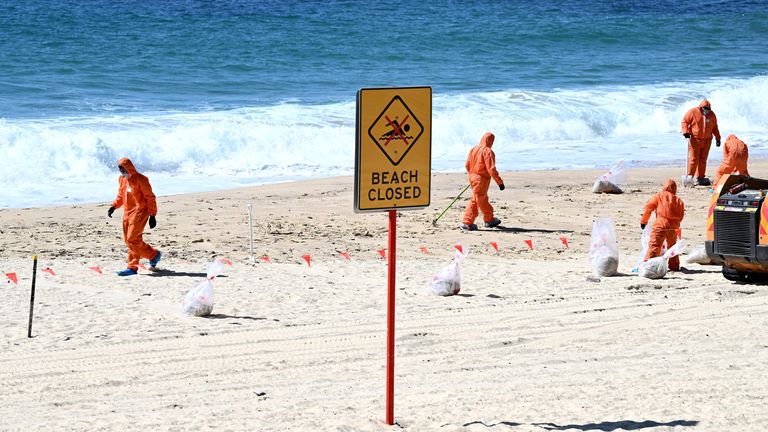 Werknemers in beschermende kleding ruimen onbekend puin op dat is aangespoeld op Coogee Beach, Sydney, Australië.  Foto: AAP/Reutrers