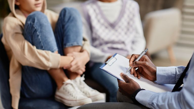 Zbliżenie na afroamerykańskiego psychologa robiącego notatki w schowku podczas sesji terapeutycznej dla dzieci. Zdjęcie: iStock