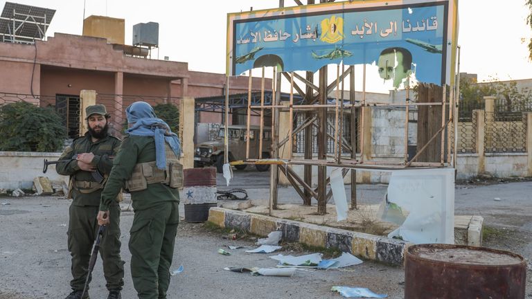 Syrian opposition fighters stand next to a government sign after entering the village of Anjara, western outskirts of Aleppo, Syria, Thursday Nov. 28, 2024, (AP Photo/Omar Albam)