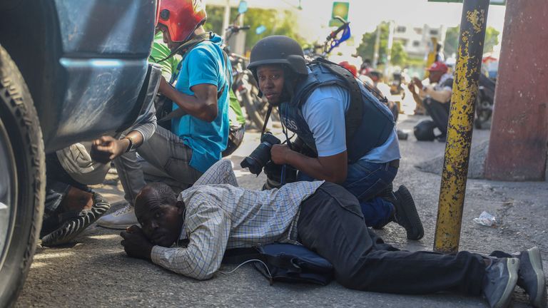 Journalists take cover from the exchange of gunfire between gangs and police in Port-au-Prince, Haiti, Monday, Nov. 11, 2024. (AP Photo/Odelyn Joseph)