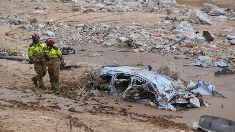 Rescue workers pass a destroyed half buried car after floods in Paiporta near Valencia, Spain, Sunday, Nov. 3, 2024. (AP Photo/Hugo Torres)