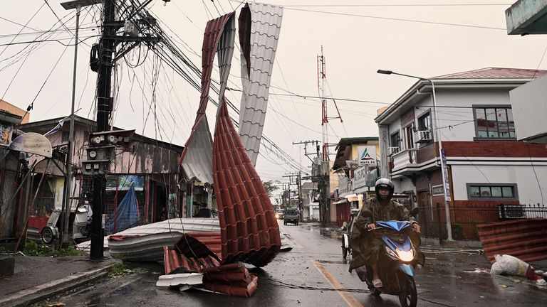 Motorists ride past a part of a roof suspended on electric wires blown by strong winds caused by Typhoon Man-yi along a street in the municipality of Baler, Aurora province, northeastern Philippines Monday, Nov. 18, 2024. (AP Photo/Noel Celis)