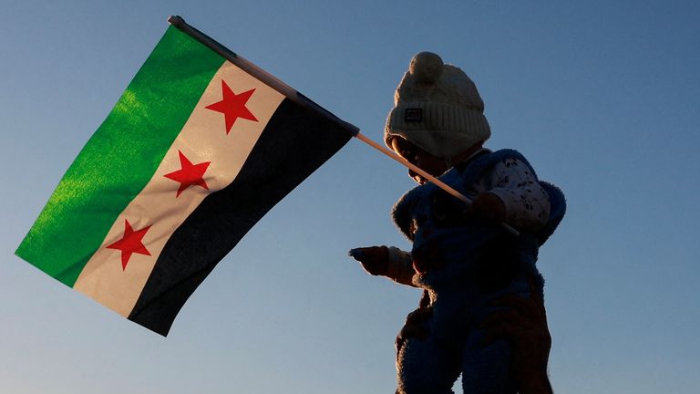 A child holding the flag adopted by the new Syrian rulers is held up in Damascus old city. Pic: Reuters

