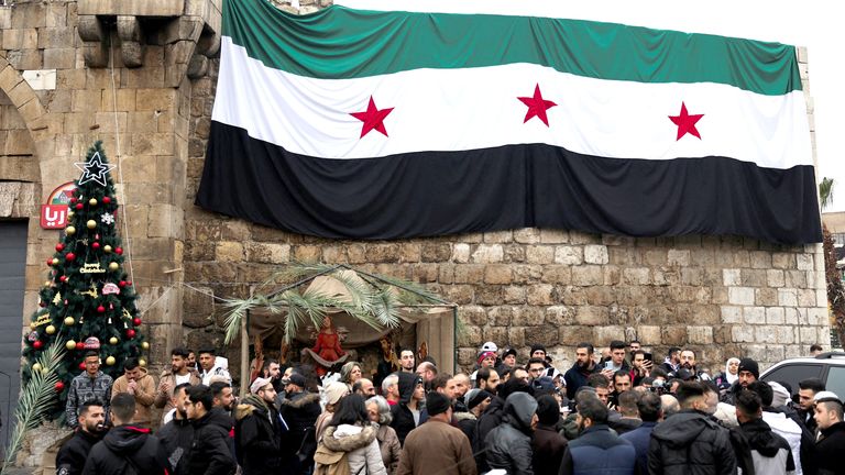 People gather near a Christmas tree and a flag adopted by the new Syrian rulers, on the day of a protest against the burning of the Christmas tree in Hama, at Bab Touma neighbourhood in Damascus, Syria December 24, 2024. REUTERS/Amr Abdallah Dalsh