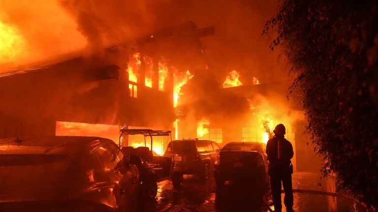 A firefighter sprays water on a home as it burns in the Franklin Fire in Malibu, California., Tuesday, Dec. 10, 2024. (AP Photo/Jae C. Hong)