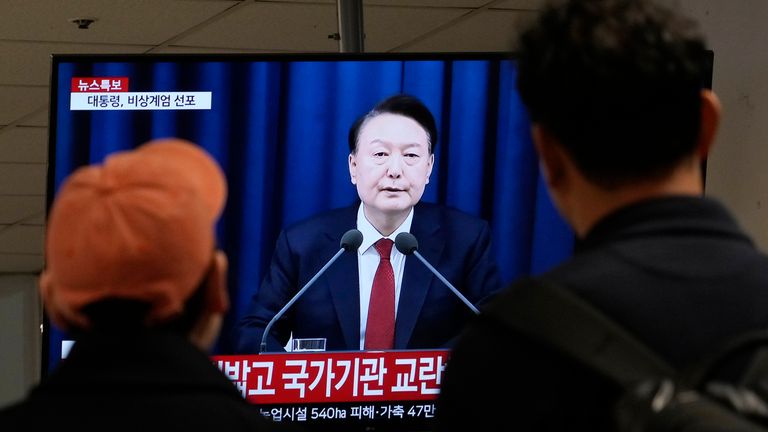 People watch South Korean President Yoon Suk Yeol's televised address  at a bus terminal in Seoul, South Korea.
Pic: AP