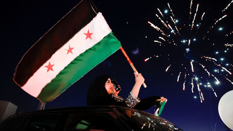 A woman holds up the flag adopted by the new Syrian rulers, as people celebrate after fighters of the ruling Syrian body ousted Syria's Bashar al-Assad. Pic: Reuters