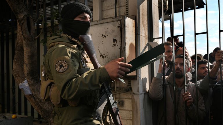 A Syrian fighter, left, stands guard as members of ousted Syrian President Bashar Assad's army line up before registering their names with Syrian rebels as part of an "identification and reconciliation process" in Damascus, Syria, Monday, Dec. 23, 2024. (AP Photo/Hussein Malla)