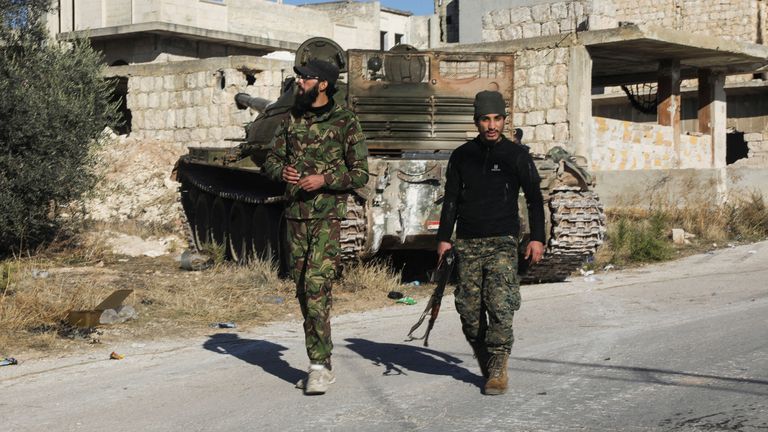 Rebel fighters walk near a military vehicle in Maarat al-Numan in Idlib province, Syria December 1, 2024. REUTERS/Mahmoud Hassano