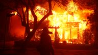 A firefighter shields their face as the Palisades Fire burns down a home in Los Angeles. Pic: AP