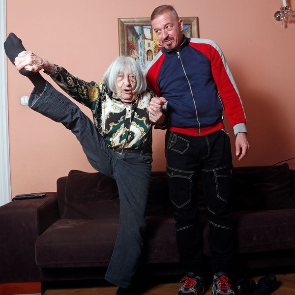 Agnes Keleti, former Olympic gold medal winning gymnast, demonstrates her flexibility as she poses for a photo with her son Rafael at her apartment in Budapest, Hungary Wednesday Jan. 8, 2020. Although she turned 99 on Thursday, even a 9-year-old would have a hard time keeping up with Agnes Keleti's irrepressible energy and enthusiasm. Keleti is the oldest living Olympic champion and a Holocaust survivor. She won 10 medals in gymnastics — including five golds — at the 1952 Helsinki Games and at 