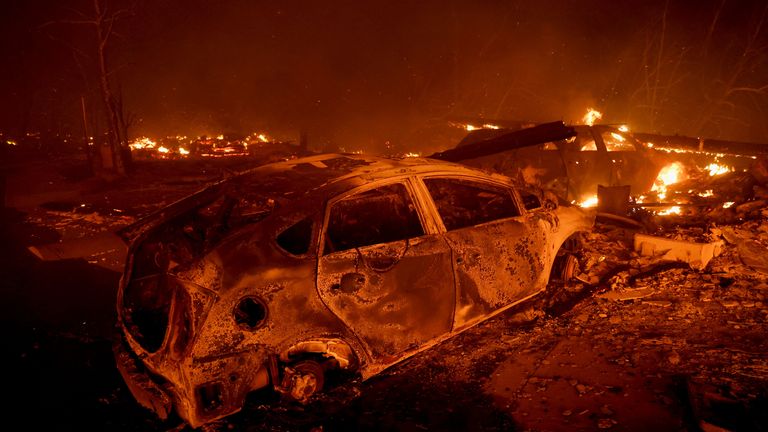 A burnt vehicle remains as flames rise nearby, as the Eaton Fire burns in Pasadena, California, U.S. January 7, 2025. REUTERS/Mario Anzuoni