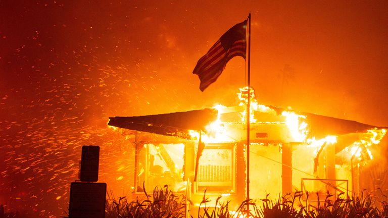 Een Amerikaanse vlag wappert terwijl vuur een gebouw overspoelt terwijl het Palisades Fire brandt tijdens een storm aan de westkant van Los Angeles, Californië. Afbeelding: Reuters 