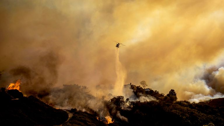 Water is dropped on the advancing Palisades Fire by helicopter in the Pacific Palisades neighborhood of Los Angeles, Tuesday, Jan. 7, 2025. (AP Photo/Ethan Swope)