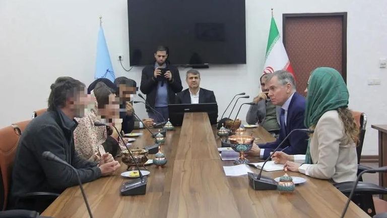 Left side of table (blurred faces of) Craig and Lindsay Foreman charged with espionage in Iran. Right side of table (in blue suit and tie) UK ambassador to Iran Hugo Shorter. Source: Iran state-run Mizan news agency https://www.mizanonline.ir/