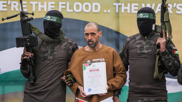 Israeli captive, Eli Sharabi, who has been held hostage by Hamas in Gaza since October 7, 2023, stands on a stage escorted by Hamas fighters before being handed over to the Red Cross in Deir al-Balah, central Gaza Strip, Saturday Feb. 8, 2025. (AP Photo/Abdel Kareem Hana)