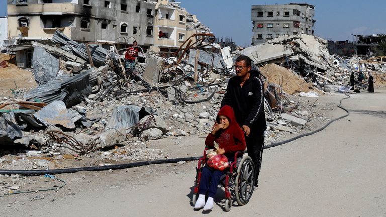 A Palestinian man pushes a child in a wheel chair past destroyed buildings. 
Pic: Reuters/Hatem Khaled