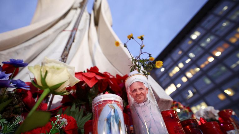 A candle with an image of Pope Francis lies next to the statue of late Pope John Paul II, outside the Gemelli Hospital, where Pope Francis is admitted for treatment, in Rome, Italy, February 20, 2025. REUTERS/Guglielmo Mangiapane
