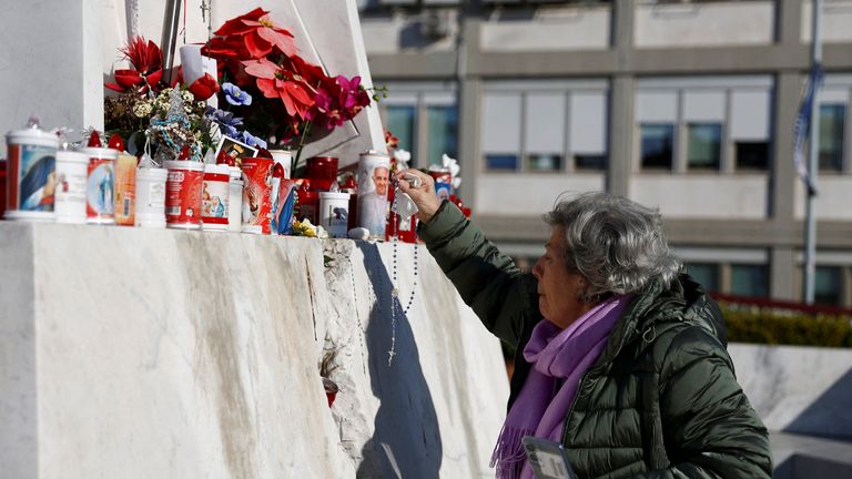 A woman places a rosary at the statue of the late Pope John Paul II outside Gemelli Hospital, where Pope Francis is admitted for treatment, in Rome, Italy